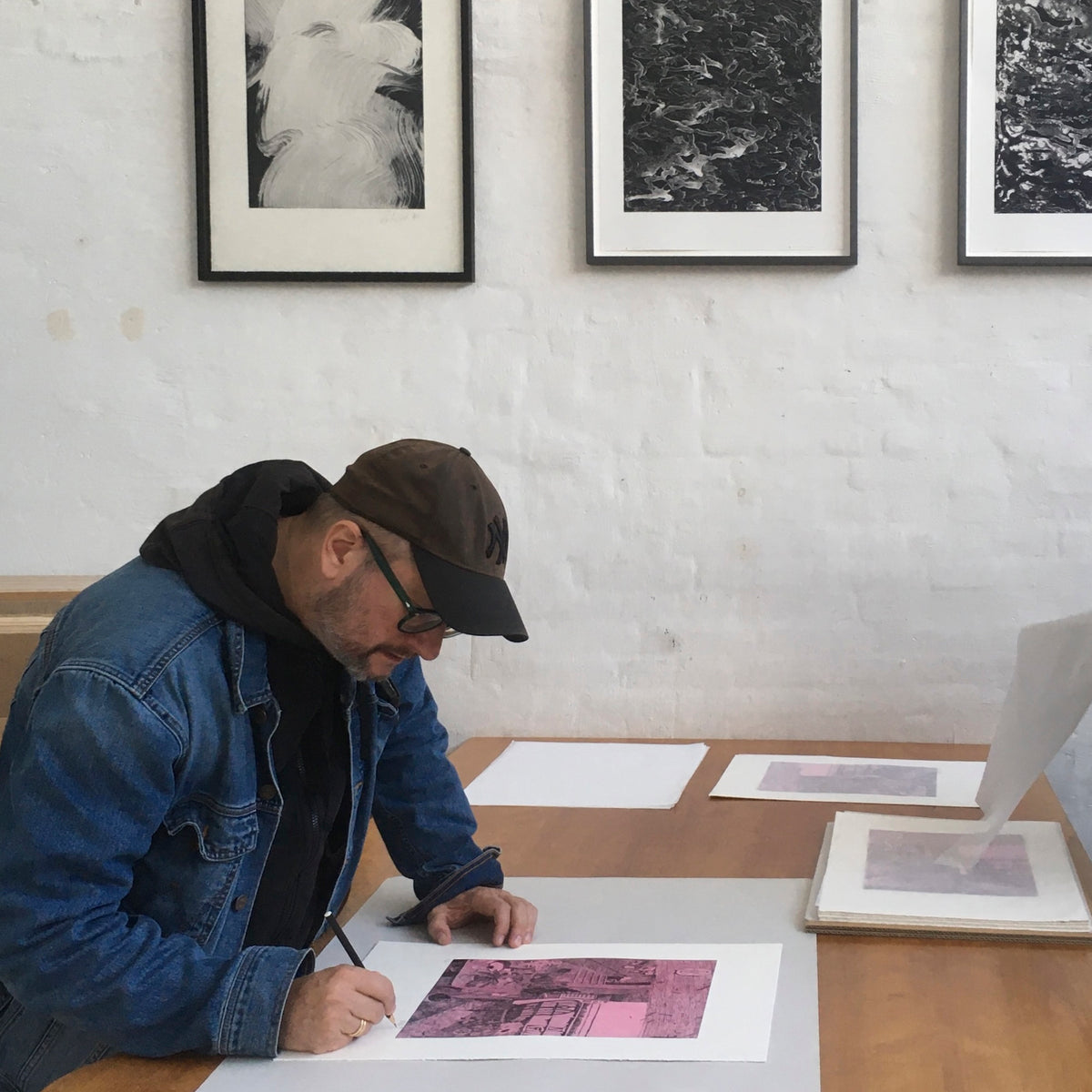 Artist Morten Schelde signs his pink etching "Ocean of Time" while leaning over a Printer's Proof studio table.
