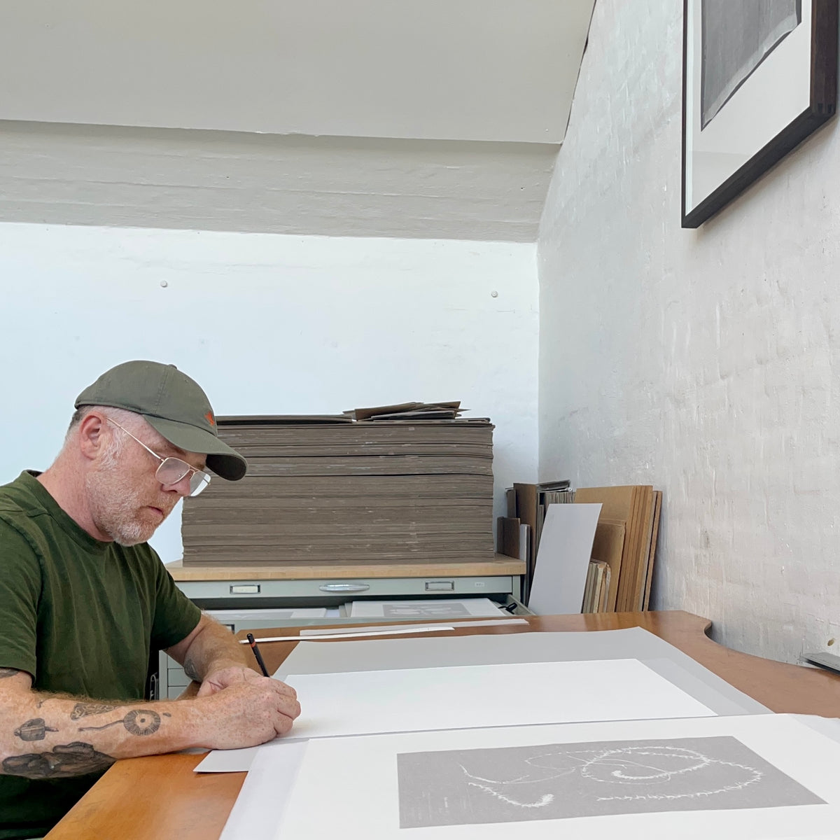 Artist Nicolai Howalt sitting at a studio table, signing his limited-edition photo etching series.